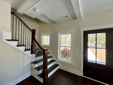 Modern staircase with dark wood steps and black metal railing near a bright entry door.