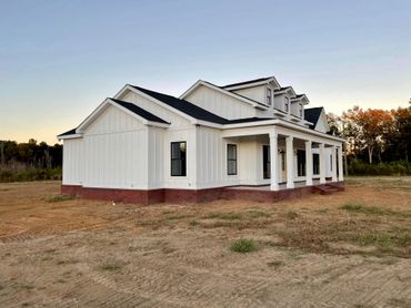 Newly built white farmhouse with a wraparound porch in a rural setting.