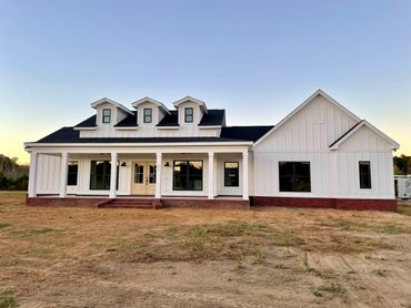 Modern white farmhouse with three dormer windows and a spacious porch.