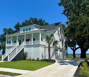 Modern white house with a porch and palm trees under a clear blue sky.