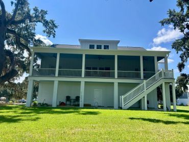 Elevated two-story house with a spacious porch and staircase under a clear blue sky.