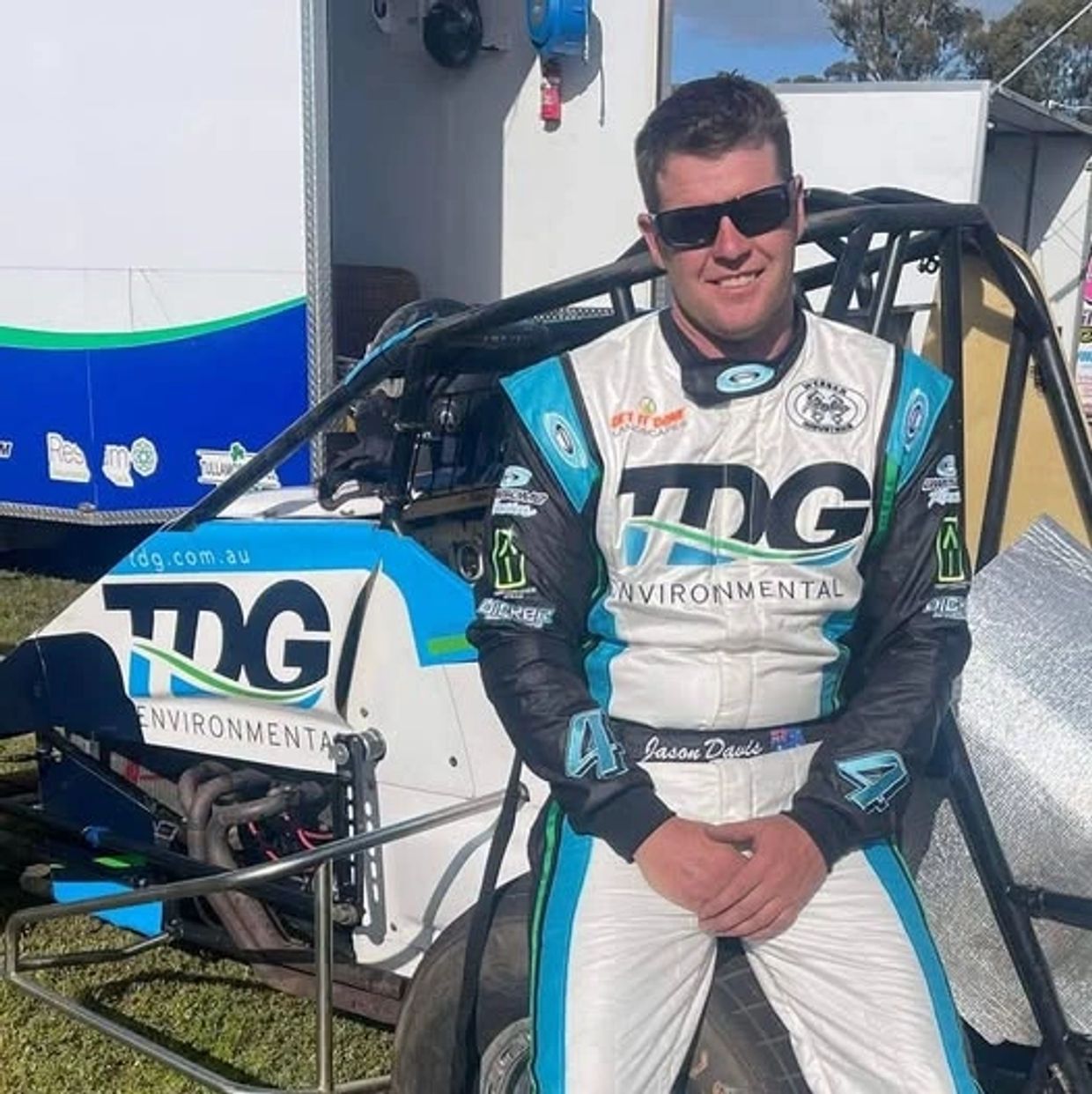 Race car driver in blue and white suit posing by his car.