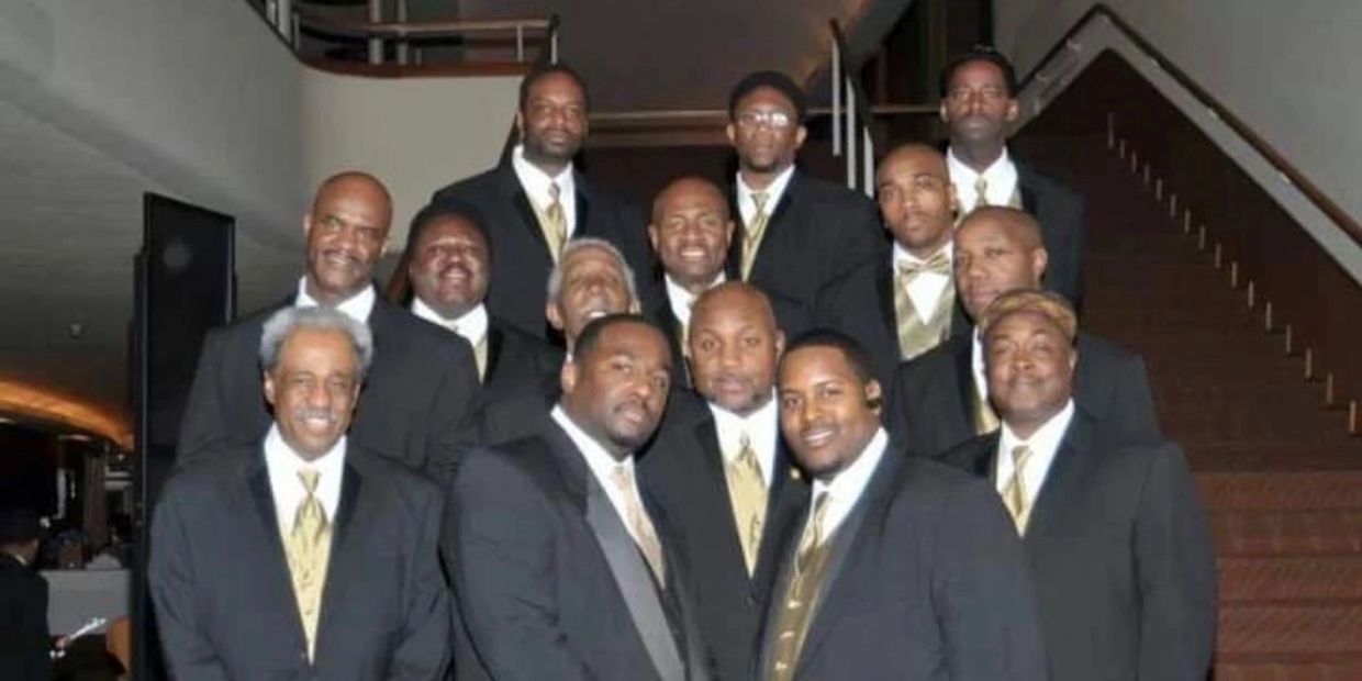 Group of men in black suits and gold ties posing for a photo.