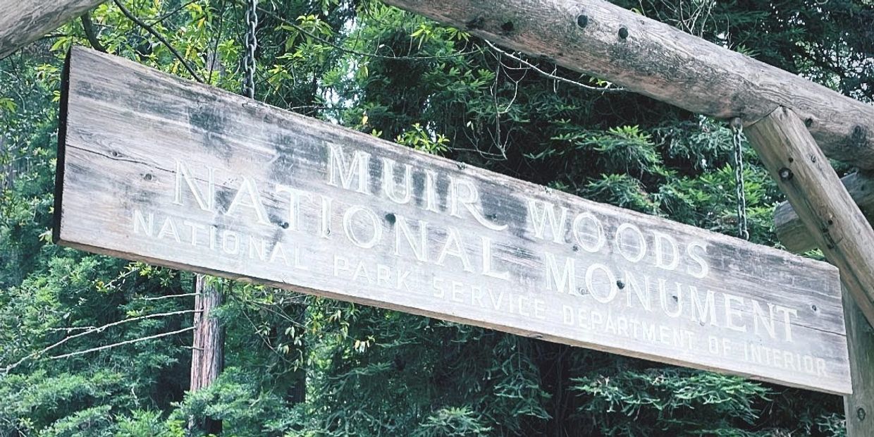 A hanging wooden sign at the entrance of Muir Woods National Monument, California.