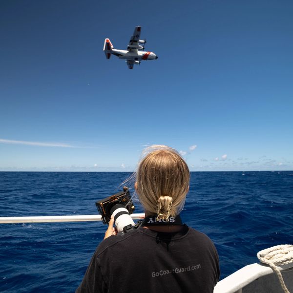 Person on boat photographing a plane over the ocean.