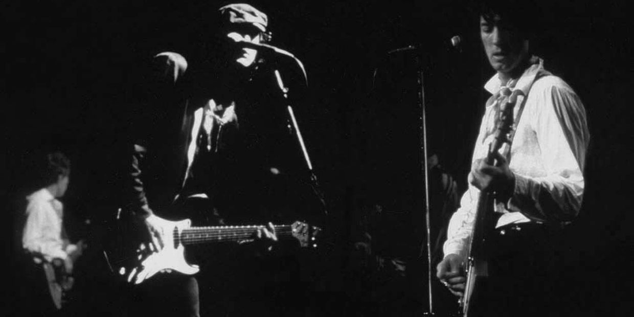 Black and white photo of musicians playing electric guitars on stage.