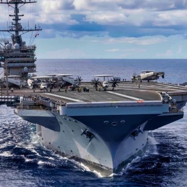 Aircraft carrier sailing on the ocean with planes on deck.