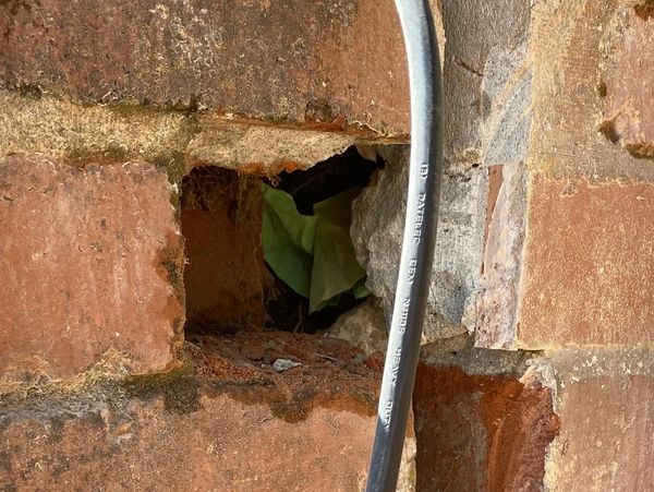 Damaged brick wall with missing bricks and cable running through.