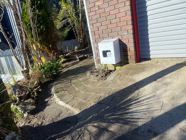 Garden path alongside a brick wall with a utility box.