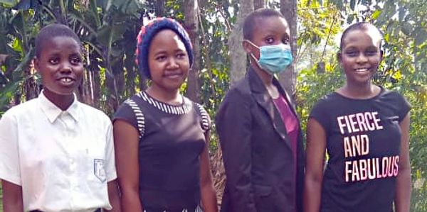 Four young women standing outdoors with trees in the background.