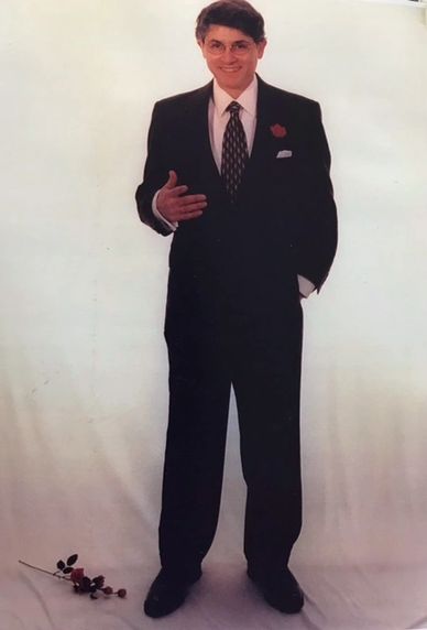 photo shoot of jack petrotto standing with black suite, white background, ans a single red rose on t