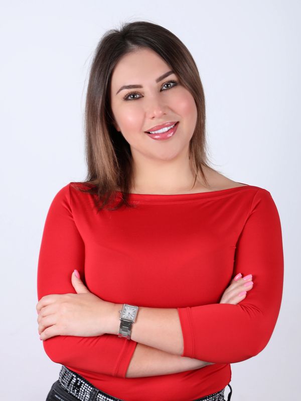 Woman smiling confidently with arms crossed, wearing a red top and black jeans.