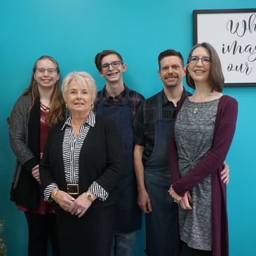 Five people smiling in front of a sign on a turquoise wall.