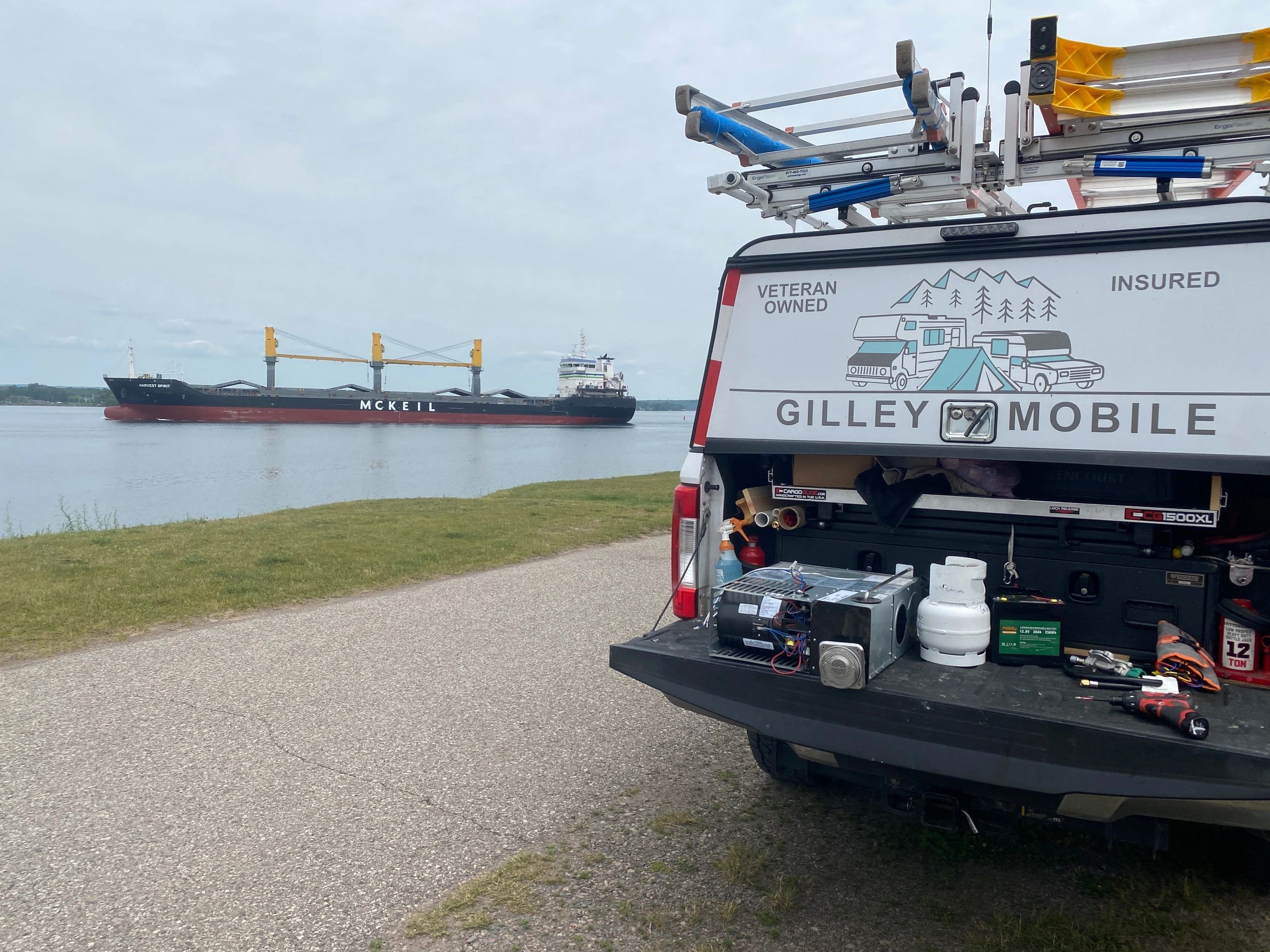 Gilley Mobile RV Service working in Sault Ste. Marie on the St. Mary' River as a ship passes by.