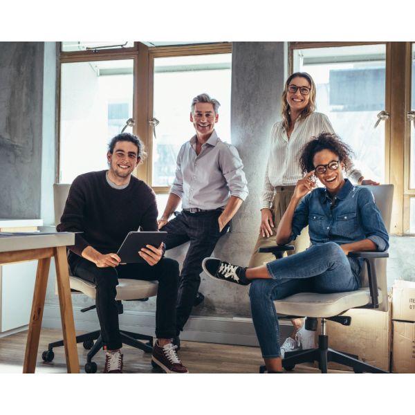A diverse group of four young professionals smiling in a modern office.