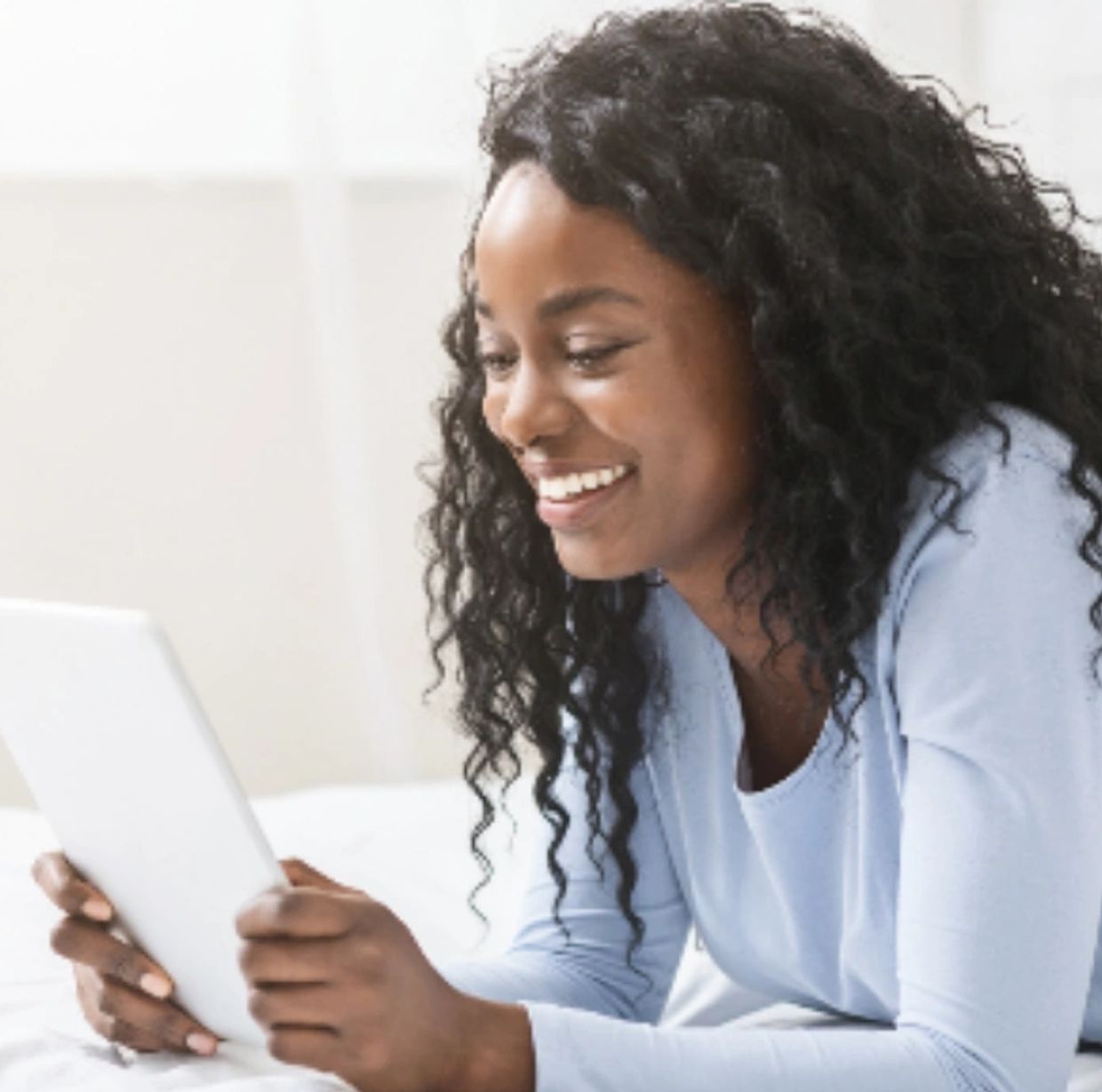 Woman smiling while using a tablet in bed.