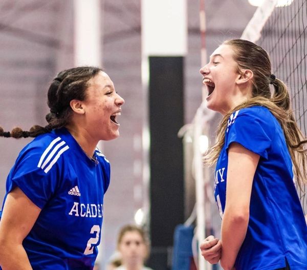 Two female volleyball players in blue jerseys celebrating joyfully.