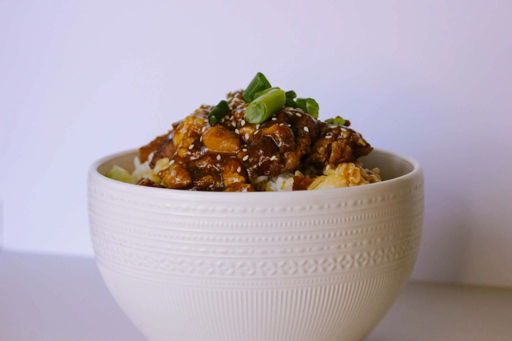 Bowl of savory rice topped with meat, sauce, cashews, and green onions.