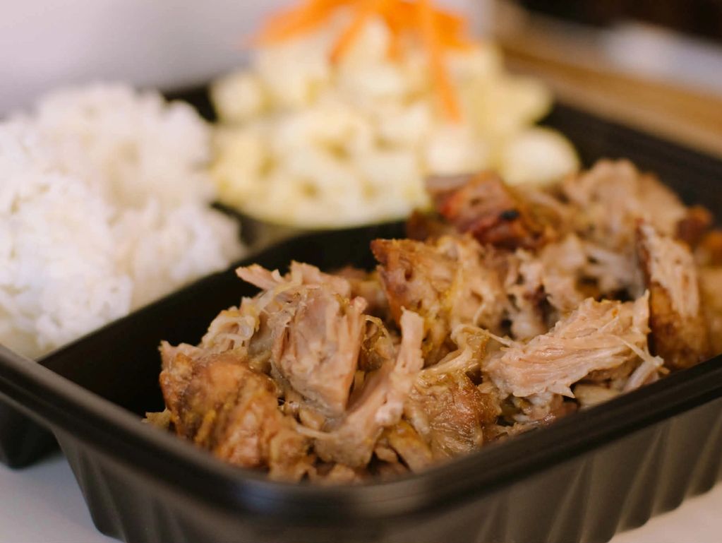 A close-up of a meal with shredded meat, rice, and a side dish in a black container.