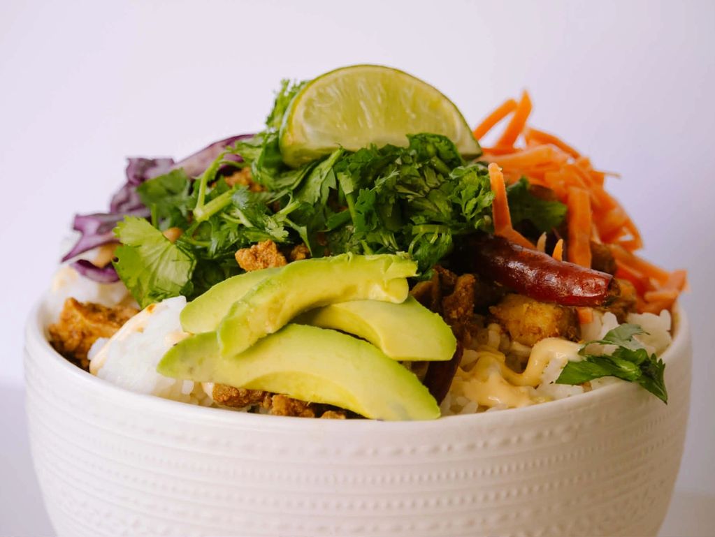 A fresh bowl with avocado, rice, herbs, and shredded carrots.
