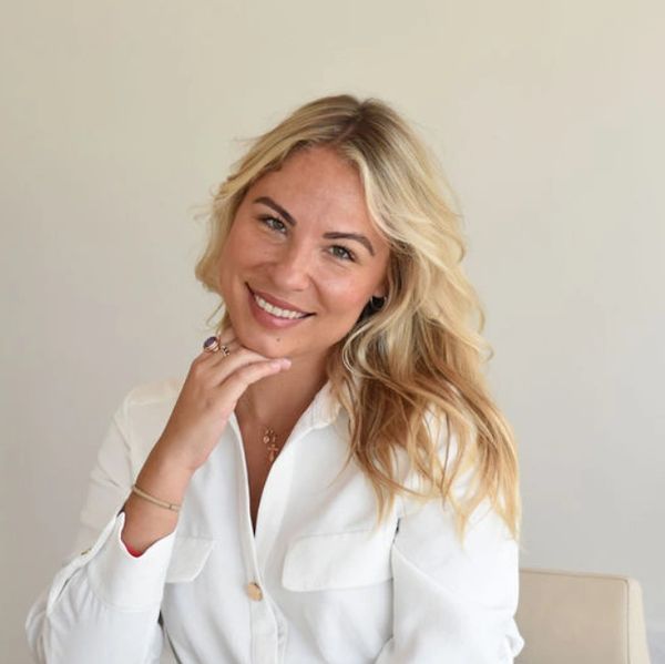 Smiling woman with blonde hair in a white blouse, posing with hand near face.