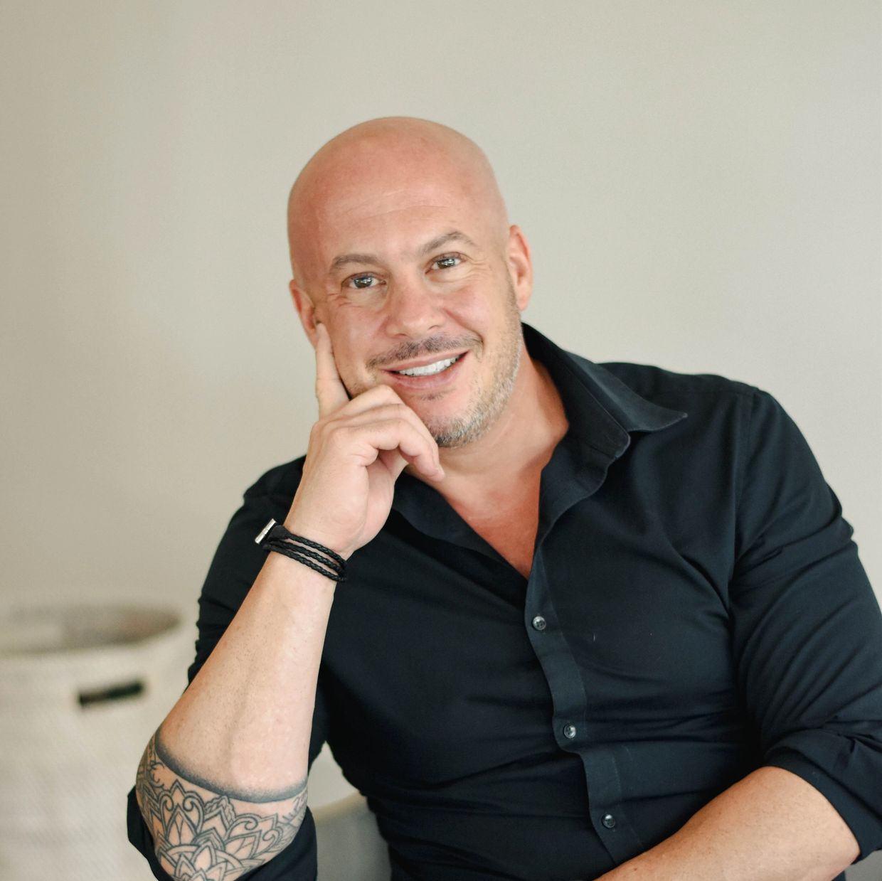 Smiling bald man with a tattoo on his forearm wearing a black shirt.