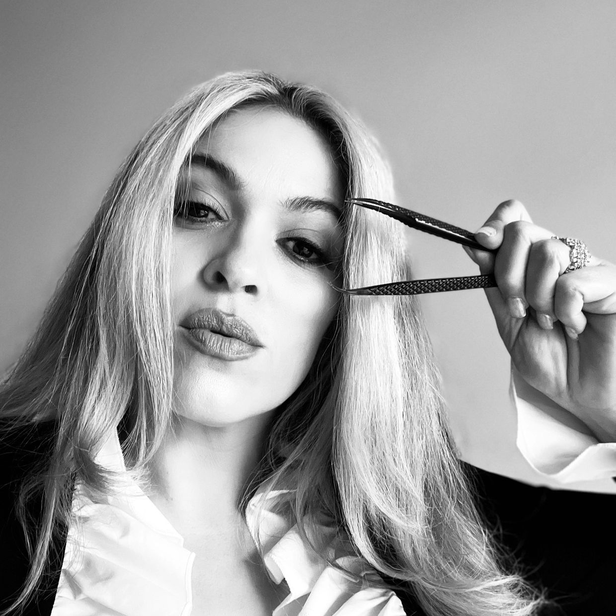 Black and white portrait of a woman holding tweezers near her face.