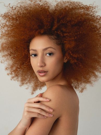 Woman with voluminous curly red hair posing gracefully.