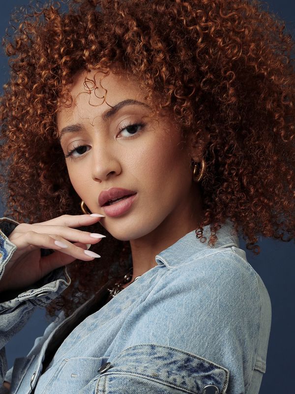 Woman with curly hair in a denim jacket.
