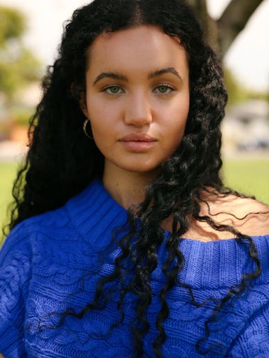 Young woman with curly hair wearing a blue sweater outdoors.