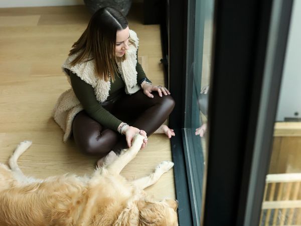 Woman sitting by window holding dog's paw.