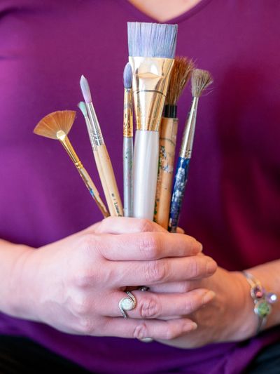 Woman's hands holding paintbrushes against a plum background
