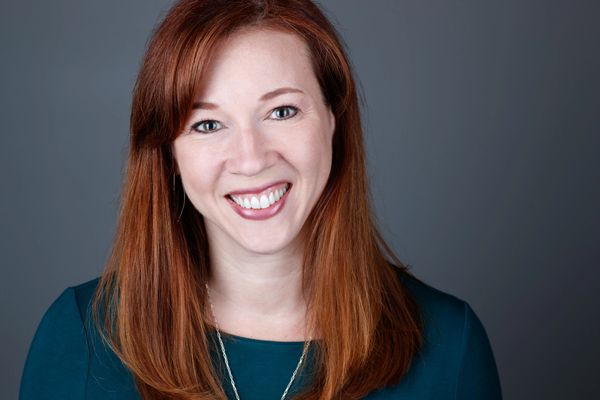 Smiling woman with red hair is a headshot of Elaina Whittenhall