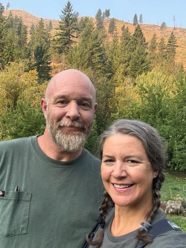 Smiling couple outdoors with forest and hills in the background.