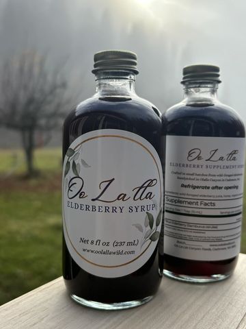 Two bottles of Oo La Lla elderberry syrup on a wooden surface outdoors.