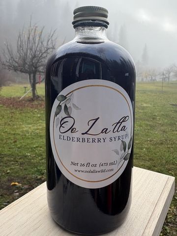 A bottle of Oolalla elderberry syrup on a wooden surface outdoors.