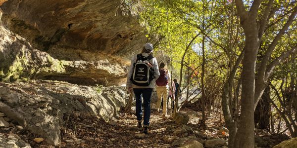 People hiking on a forest trail beside large rocks.
