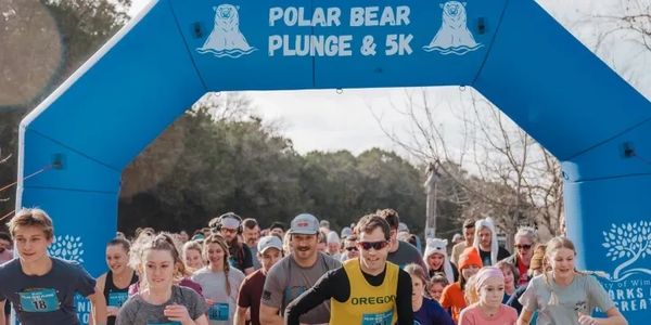 Runners starting the Polar Bear Plunge &amp; 5K event under a blue arch.