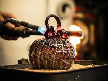 Glassblower heating a glass pumpkin with a torch.
