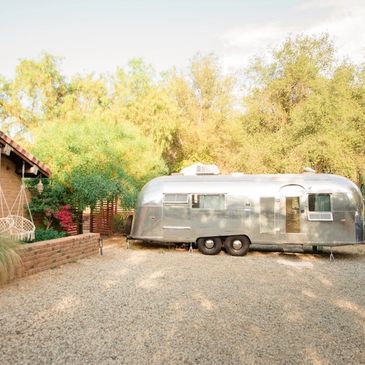 Silver trailer parked in a sunny, tree-lined yard.