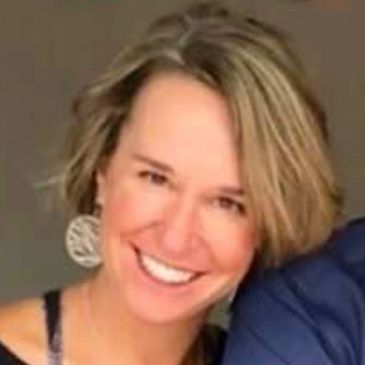 Smiling woman with short blonde hair and large circular earrings.