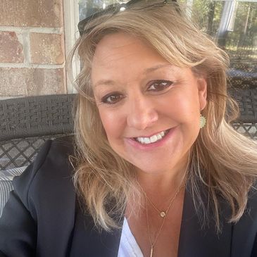 Smiling woman in a black blazer sitting outdoors.