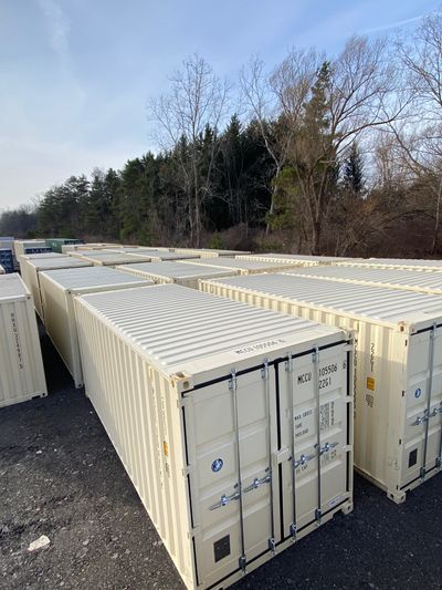 Rows of beige shipping containers lined up outdoors near trees.