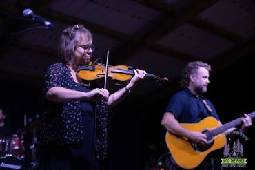 Musicians performing live with a violin and guitar on stage.