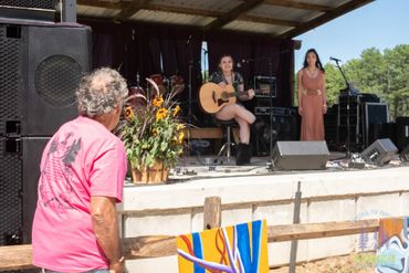 An older man watches two women performing on an outdoor stage.