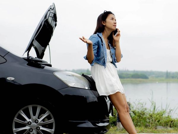 A woman standing in front of car and talking with the phone