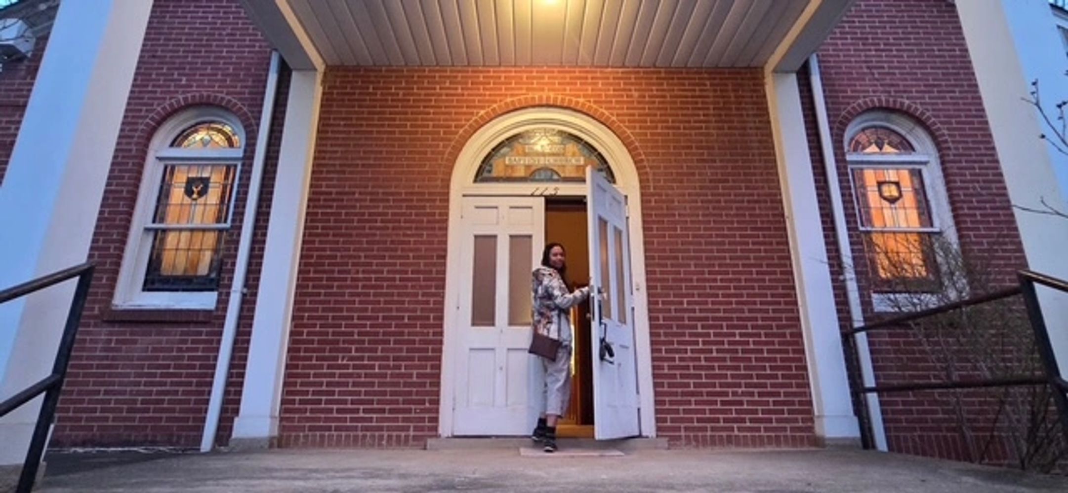 Person entering a brick building through white double doors at dusk.