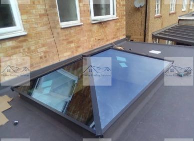Modern triangular skylight on flat roof beside brick building.