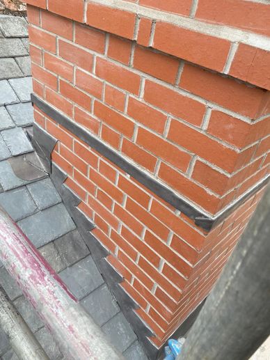 Brick chimney with metal flashing on a roof.
