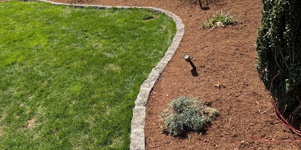 Lawn with stone border separating grass and mulched garden bed.